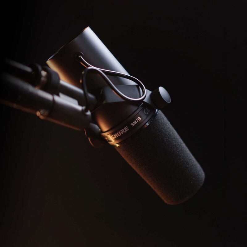 Close-up of a Shure SM7B dynamic microphone on a boom arm with a foam windscreen in a dark studio setting
